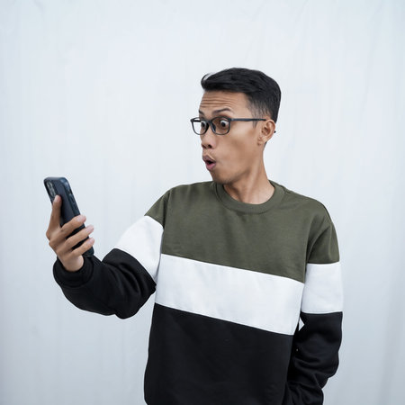 A young Asian man with glasses wearing a sweater with a surprised happy expression getting a...