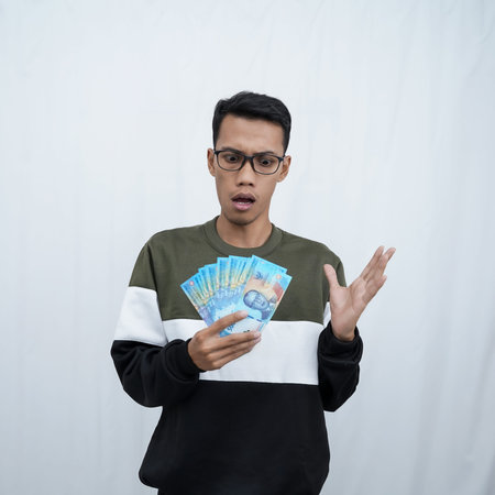 An asian young man with glasses wearing a sweater with a happy expression while carrying money,...
