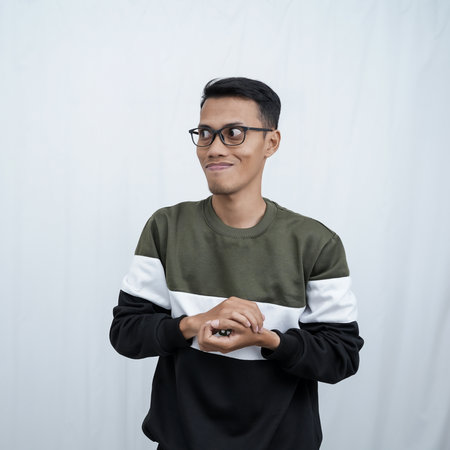 An Asian young man with glasses wearing a sweater with an expression of thinking. Isolated on white background.の写真素材