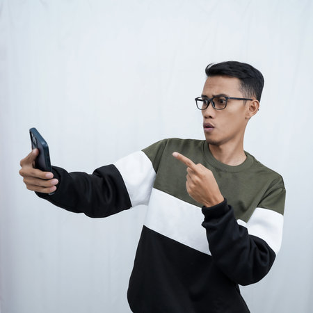 A young Asian man with glasses wearing a sweater with a surprised happy expression getting a...