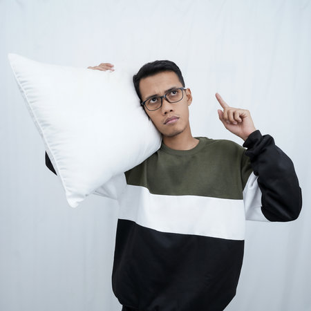 A young Asian man with glasses holding and enjoying a pillow. Isolated on white background.の写真素材