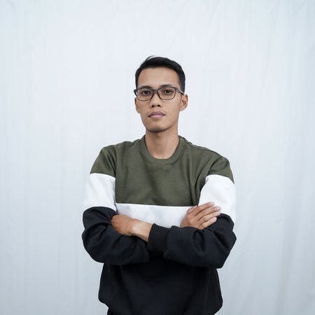 A young Asian man with glasses wearing a sweater poses standing with his arms crossed. Isolated on white background.の写真素材