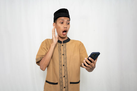 A young man in traditional clothing looking surprised while holding a phone