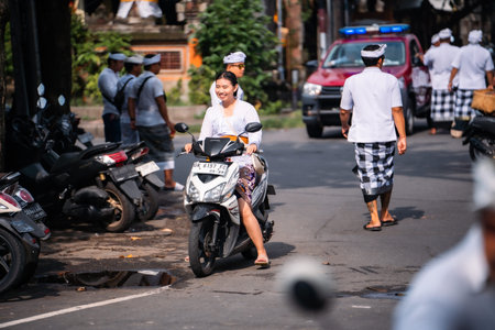 Bali, Indonesia - 08 March 2024: Beautiful woman in traditional Balinese dress riding a motorbike on...