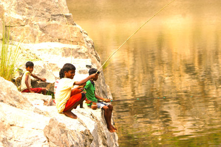Happy village tribal children fishing from a rock at morning sunny timeの写真素材