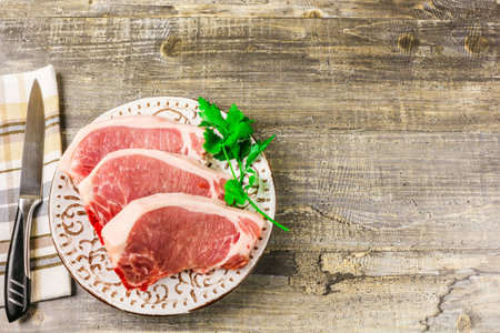 A white plate of raw sliced meat on wooden table, top view. Food, a knife, branches of greensの写真素材