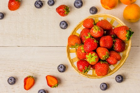 Basket of strawberries on a white wooden old table and berries on the edge of blueberries in a glass, apricots. Desktop background. advertising space. Food and drink. Top view. Dietの写真素材