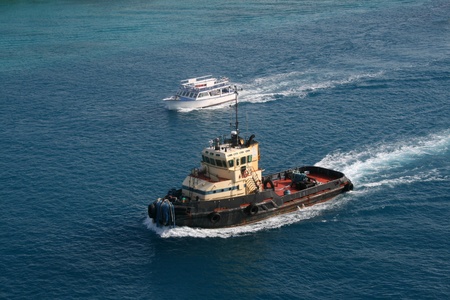 A colorful harbor tug is overtaken along a waterway by a smaller pleasure boat.の写真素材