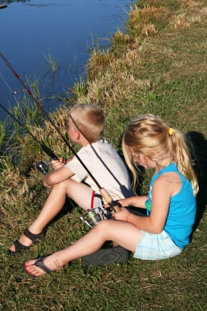 A young boy and girl fishing together on the bank of a rural farm pond のeditorial素材