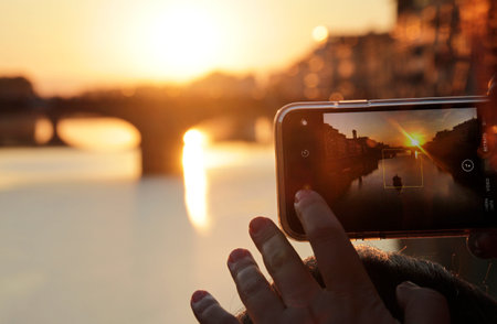 A woman uses her smartphone to take a photo of a sunset in Florence, Italy