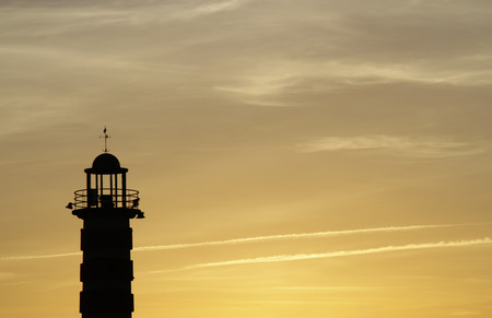 A lighthouse stands out against the golden sky during a sunset in Lisbon, Portugalの写真素材