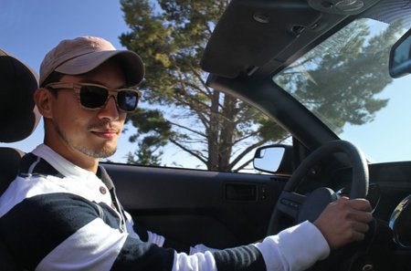 Young man with wooden sunglasses and baseball cap driving a convertible