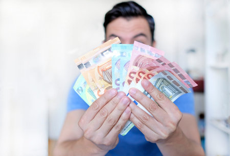Young man holding up multiple euro billsの写真素材