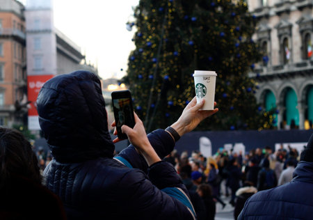 Milan, Italy - December 14, 2018: A young man holds up a Starbucks paper cup and takes a photo of it...