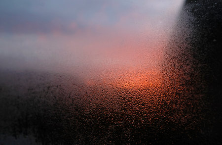 Close-up of condensation on a window with a sunset or sunrise in the backgroundの写真素材