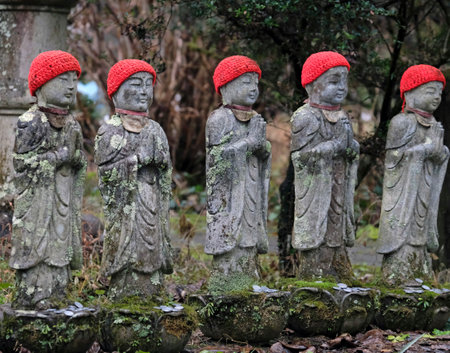 Stone statues with red hats at a temple in Japanの写真素材