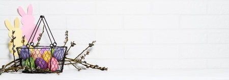 Arrangement of basket with multi colored eggs, paper rabbits and willow branches