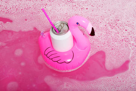 Inflatable flamingos with white can floating on a pink bath foam surfaceの写真素材
