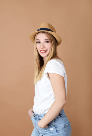 Portrait of pretty young woman with hat on beige background