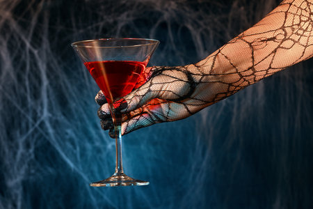 Gloved female hand with red cocktail on spiderweb backgroundの写真素材