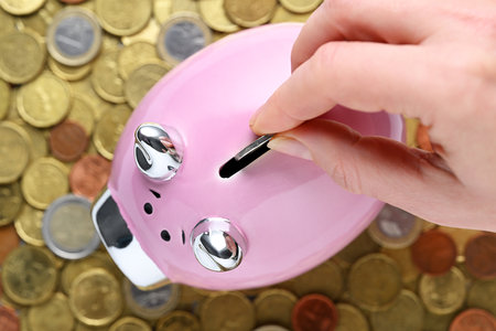 Female hand putting coin into piggy bank on many coins backgroundの写真素材