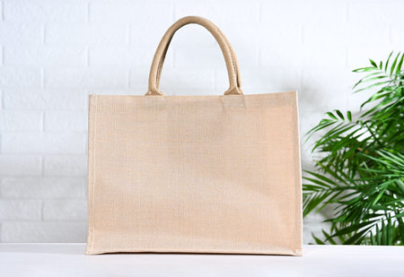 Beige canvas bag against white brick wall with palm leaves