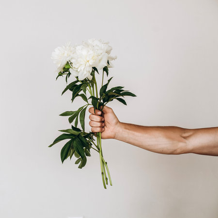 Fashion art hands of a man in summer and flowers on his hands. Creative beautiful photo of a mans hand on a light background. Skin care. Beautiful white peony. High quality photoの写真素材