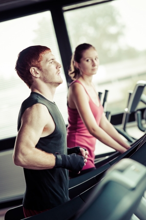 Running on treadmill in gym or fitness club - group of women and men exercising to gain more fitnessの写真素材
