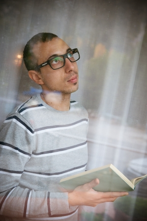 Young adult pensive man reads a book at window, Italyの写真素材