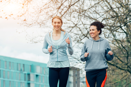 Two young female running together in city environmentの写真素材