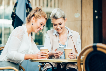 happy young women or teenage girls with smartphone and coffee cups at outdoor cafeの写真素材