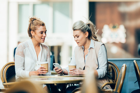 happy young women or teenage girls with smartphone and coffee cups at outdoor cafeの写真素材
