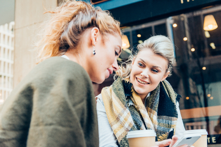 happy young women or teenage girls with smartphone and coffee cups at outdoor cafeの写真素材