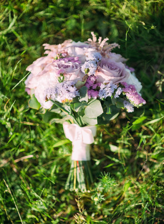 Purple bridal bouquet on green lush grass in the sun, flat lay. Classic round wedding bouquet with tender lilac flowersの写真素材