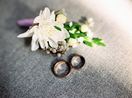 Wedding rings with groom's boutonniere, white, purple and green floral decorations on gray background. Wedding blog conceptの写真素材