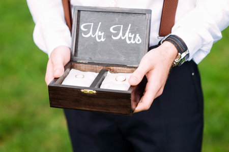 Best man holds wooden box with golden wedding rings on white pillows. Outdoor summer wedding...