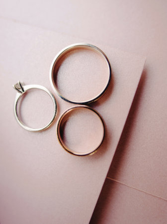 Wedding band and golden engagement ring on rosy paper background, close up, flat layの写真素材