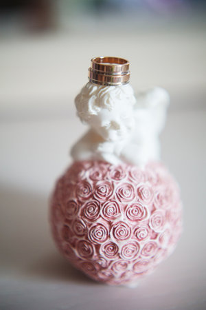 Golden wedding rings on white ceramic angel with rosy decor, eternal love conceptの写真素材