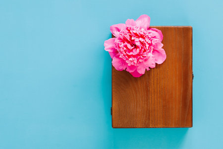 Wooden gift box with pink fresh peony on blue background. Craft box for storage pictures, top view,...