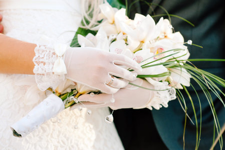 Wedding day. Bride in white gloves holds a wedding bouquet of white orchids closeup. Newlyweds,...