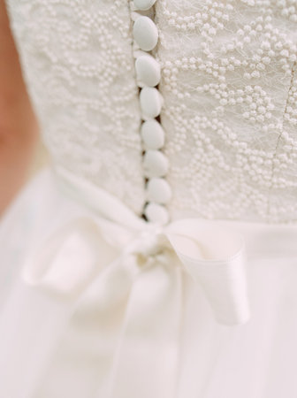 White wedding dress close up. Elegant lace, bow and small fabric-covered buttons, bridal details...