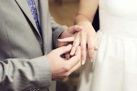 Exchange Of Wedding Rings. Wedding ceremony. Groom puts on golden wedding ring to bridal's finger, closeup. Bride and groom, newlyweds.の写真素材