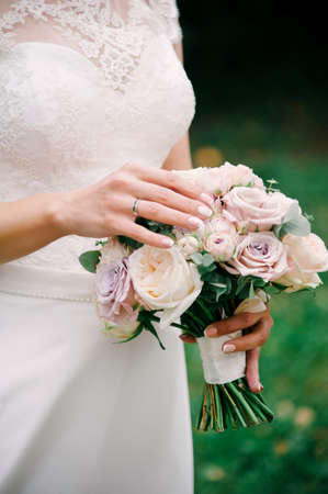 Outdoor wedding ceremony. Caucasian young bride in white lace dress holds bridal bouquet of fresh roses and peonies close up.の写真素材