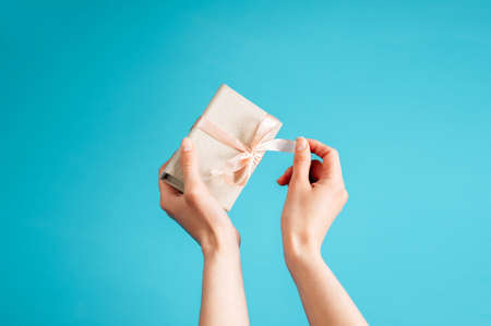Woman unpacks a gift. Woman's hands holding gift or present box decorated with pink ribbon on blue pastel table top view. Flat lay composition for birthday, Woman or Mother's day or Valentine day.の写真素材