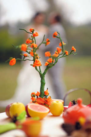 Autumn marriage. Outdoor portrait of kissing newlyweds with bright orange origami family tree in autumn park and yellow leaves. Wedding fruit table.の写真素材
