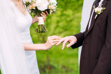 Wedding couple. Bride and fiance at outdoor wedding ceremony. Bride putting golden ring on groom's...