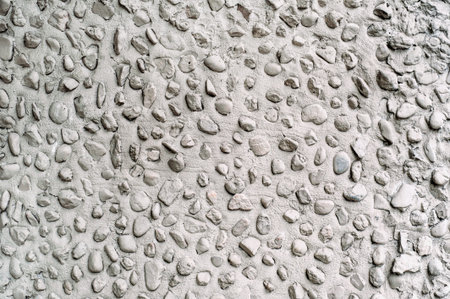 Gray cement wall with little round stones close up.