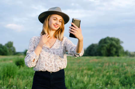 Young woman on nature using smartphone for selfie or speaking with her friends or relatives. Image for business, people, portrait, mobile and expression conceptの写真素材