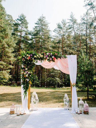 Outdoor wedding ceremony in summer pine forest. Wedding arch with floral decoration and pink fabric closeup.の写真素材