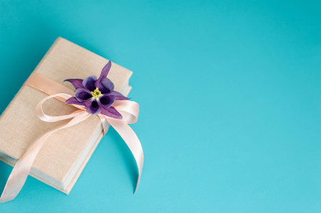 Gift box with a pink bow and purple flower on a blue background. Top view, flat lay. Template for...